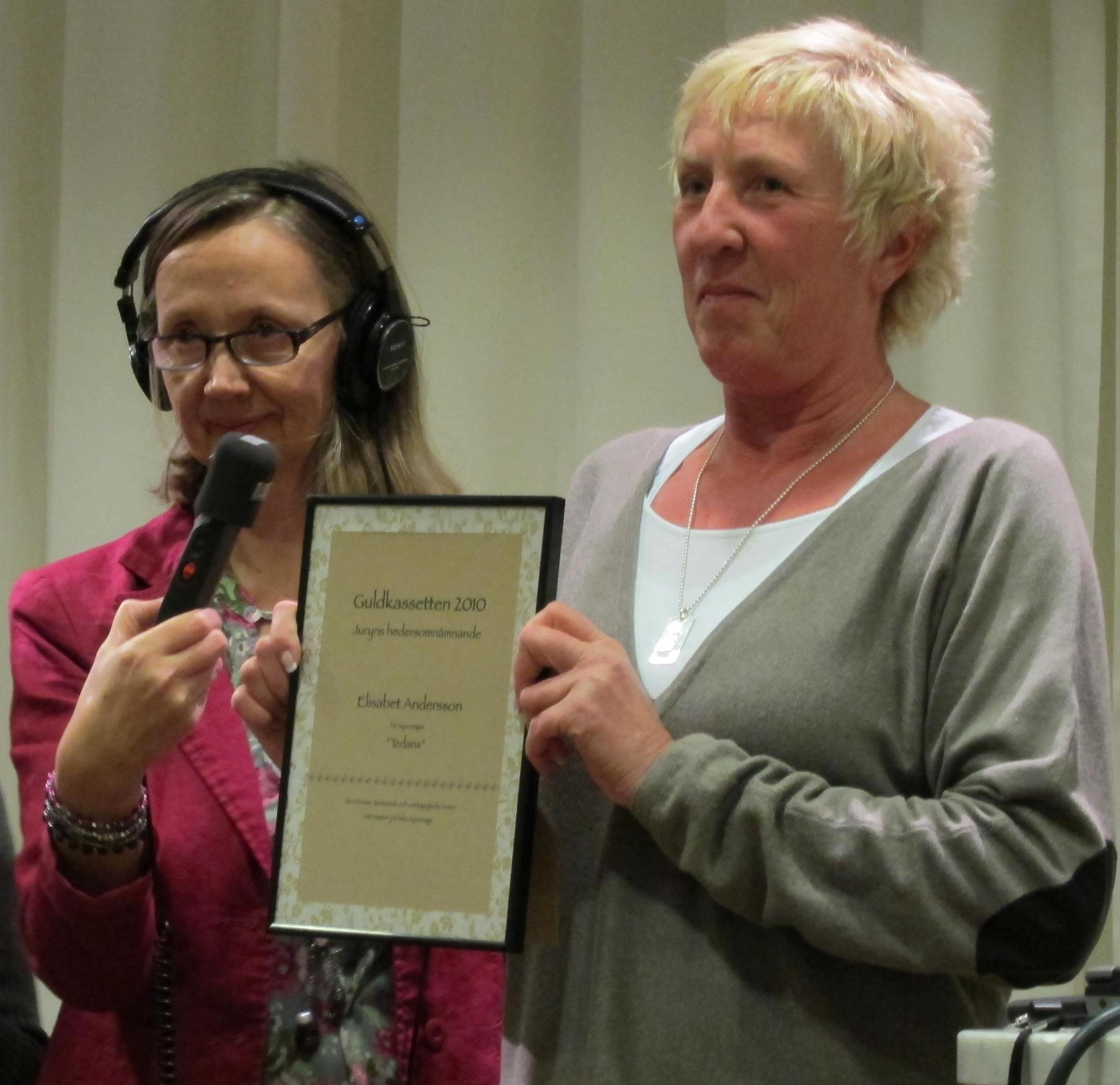 Elisabet Andersson visar upp sin plakett, medan Åsa Nilsson bandar prisutdelningen. Foto: Martin Holmström