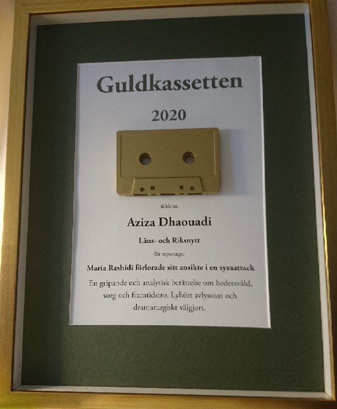 Närbild på pristavlan. En ram i guldfärg, mörkgrön passepartout och svart text på vit botten med texten "Guldkassetten 2020" överst. Under texten sitter ett guldfärgat kassettband, och under det står Aziza Dhaouadi och juryns motivering.