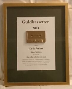 Årets Guldkassetten-tavla, med en gyllene ram, mörk passepartout och vit bakgrund. På tavlan finns förutom namn på vinnare och juryns motivering också ett gyllene kassettband.